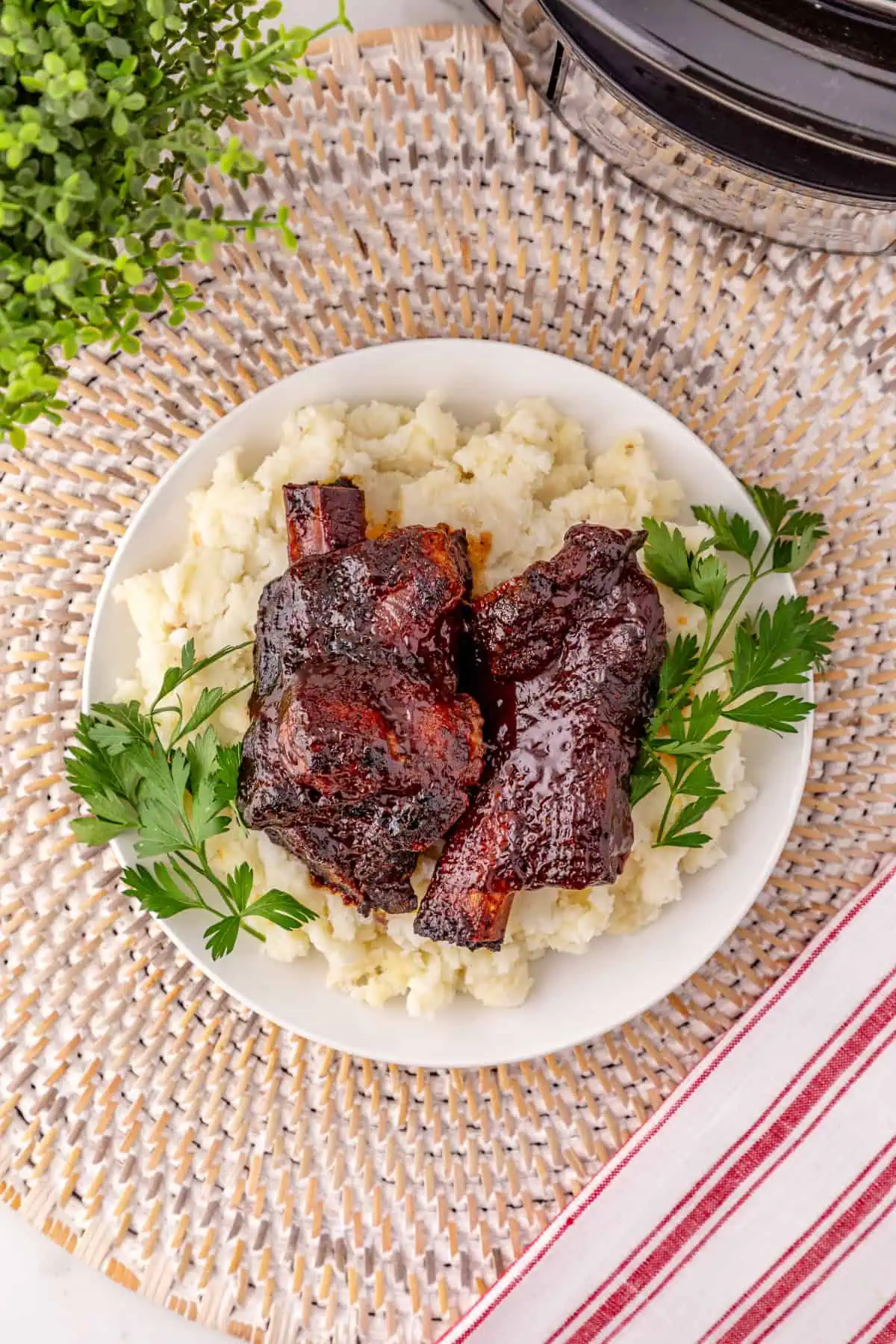 Crockpot BBQ beef ribs coated in thick caramelized barbecue sauce on a pile of mashed potatoes on a white plate with parsley to garnish