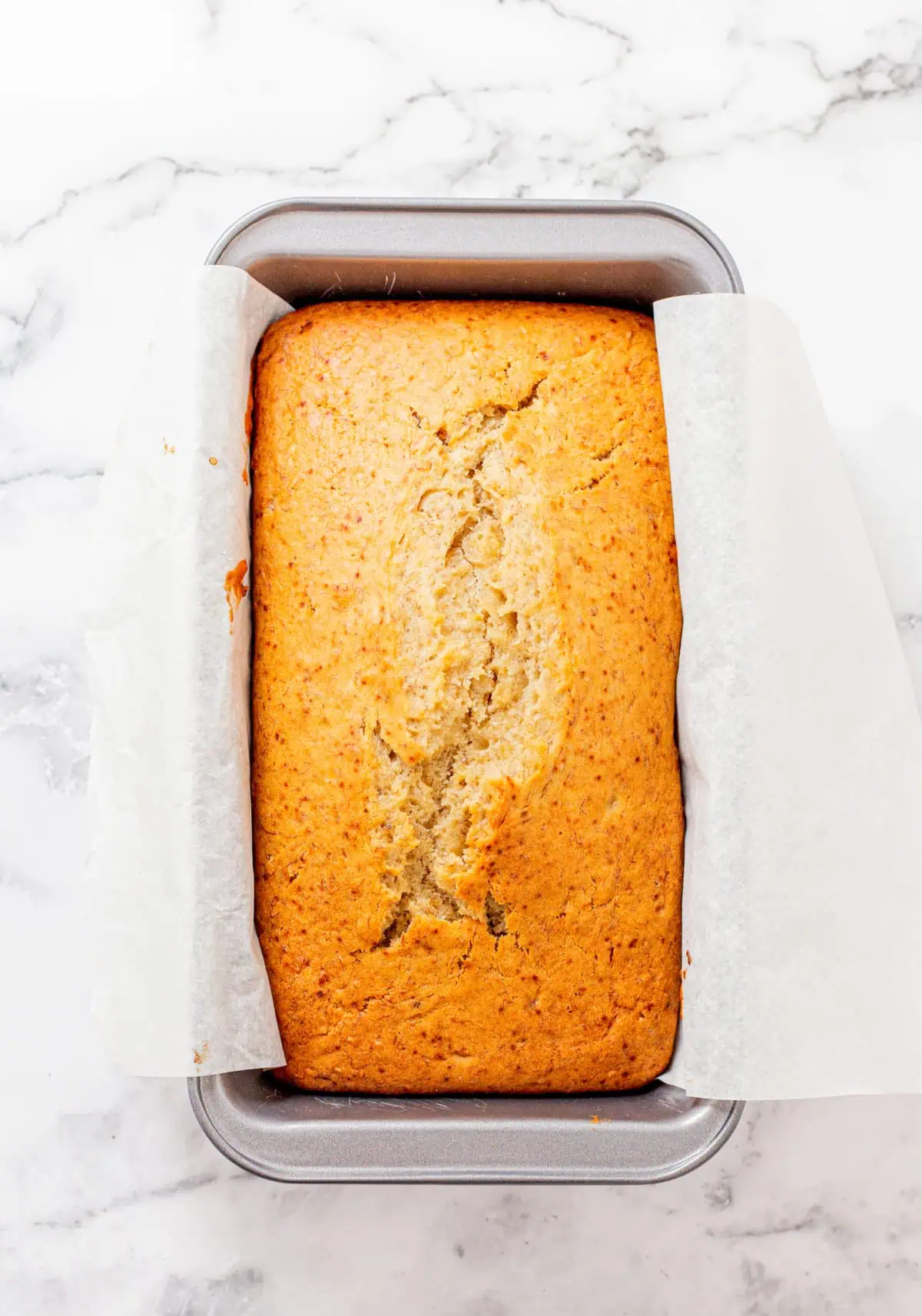 A golden loaf of moist banana bread with a cracked top on a wooden cutting board