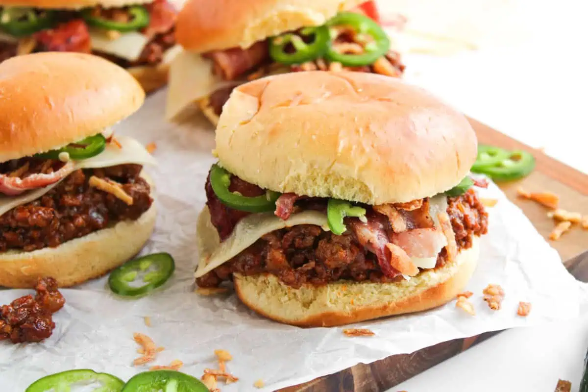 Close-up of saucy BBQ sloppy joe meat piled on a toasted bun with melty pepper jack, bacon, and jalapenos