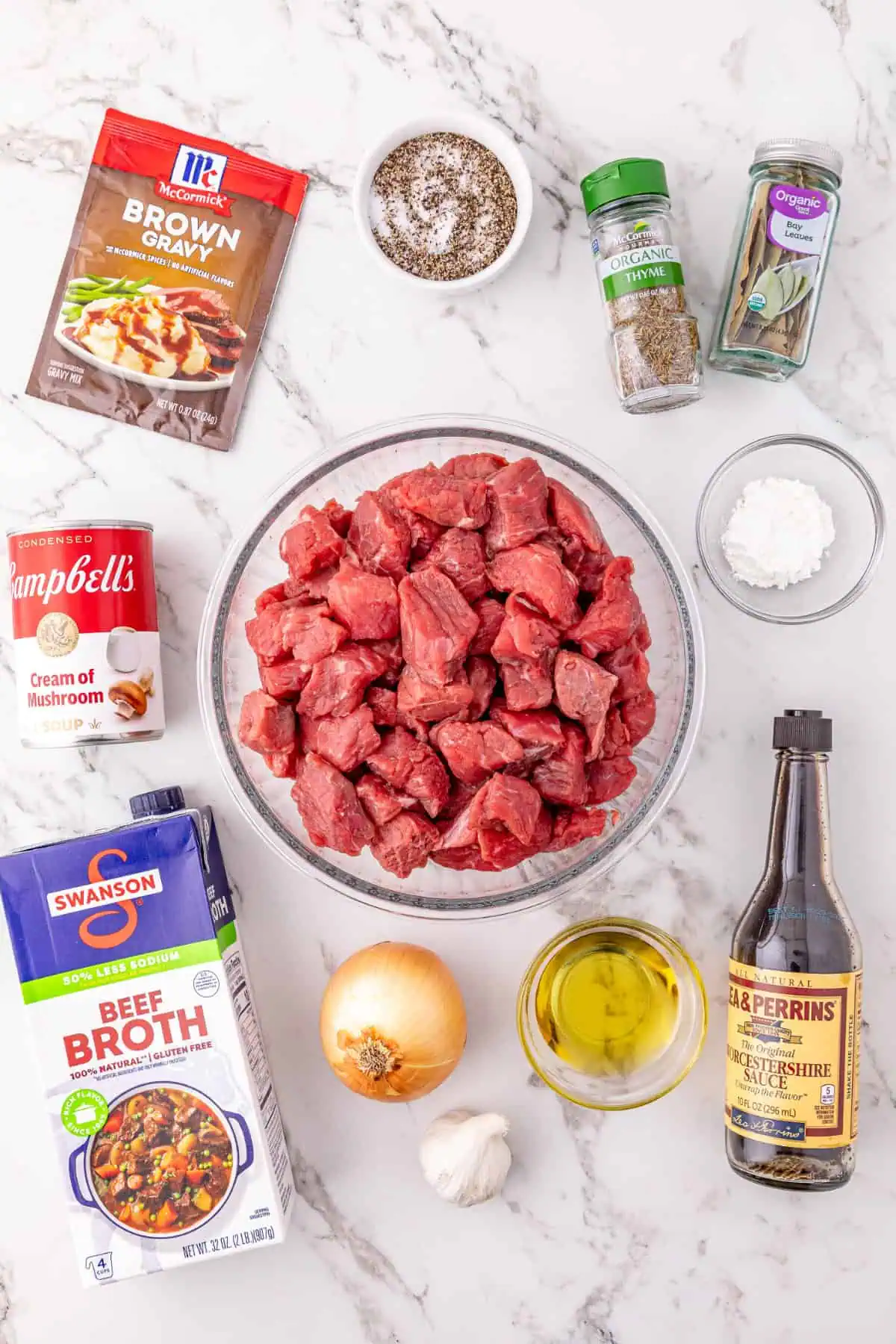 Cubed stew meat, cream of mushroom soup, a gravy packet, onion, onion, garlic bulb, worcestershire sauce, and beef broth laid out for crockpot beef tips and gravy
