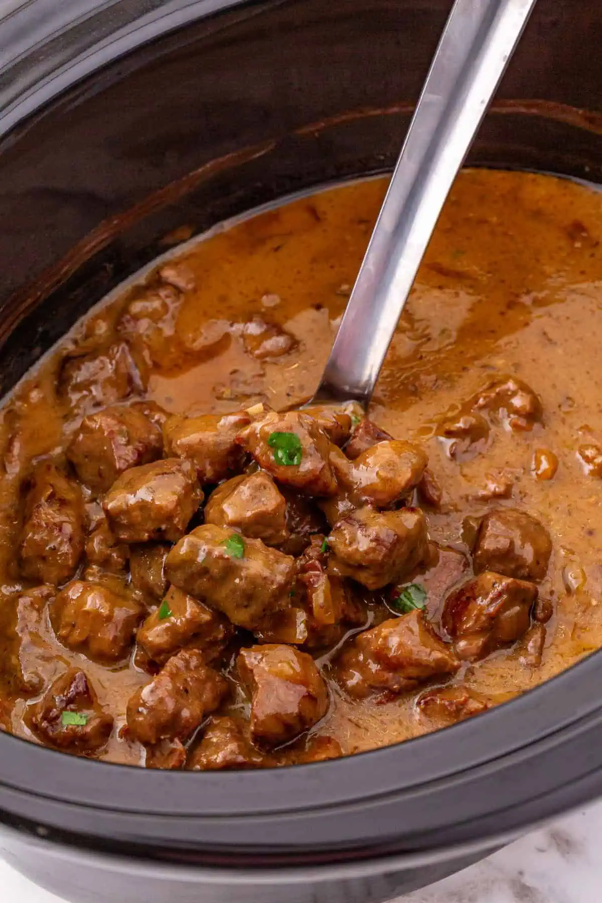 Close-up of fork-tender beef tips coated in thick, glossy mushroom gravy in a crockpot