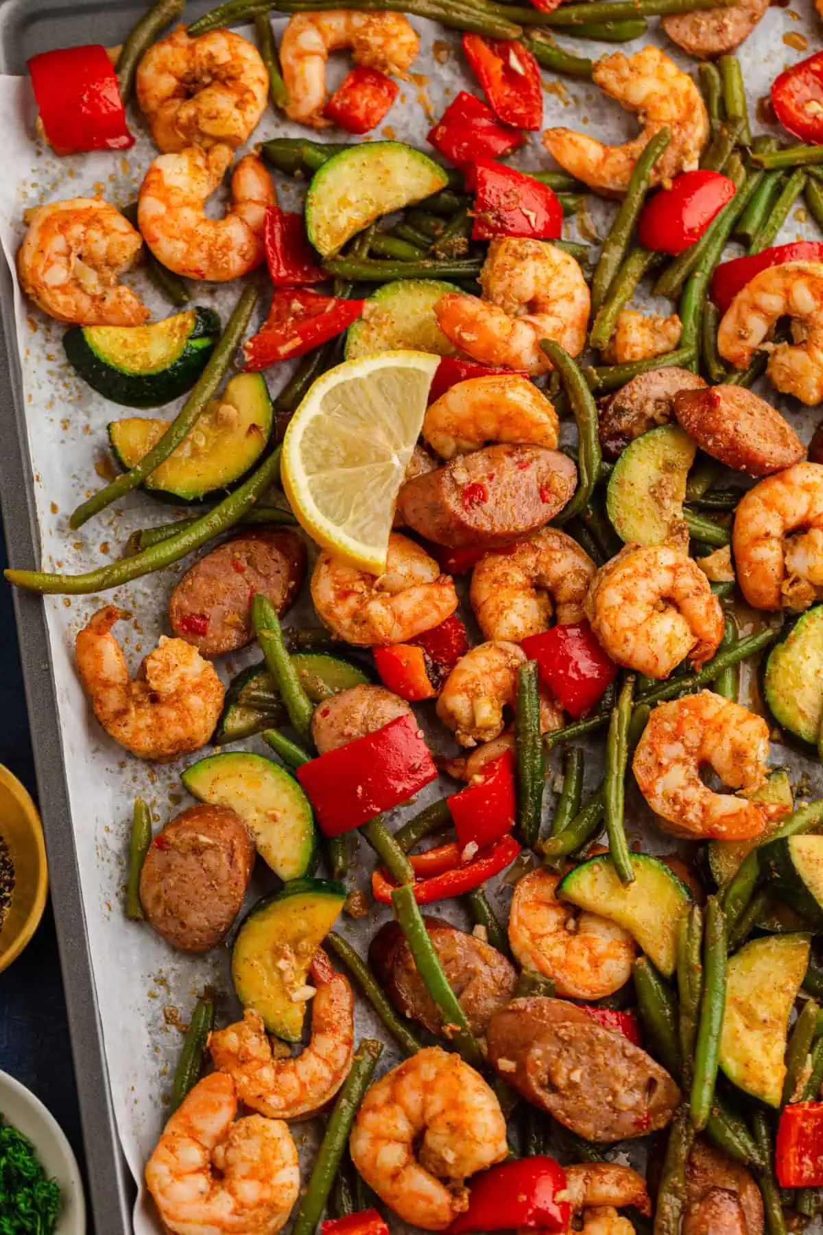 Roasted sheet pan Cajun shrimp and sausage with vegetables and lemon wedges on a sheet pan