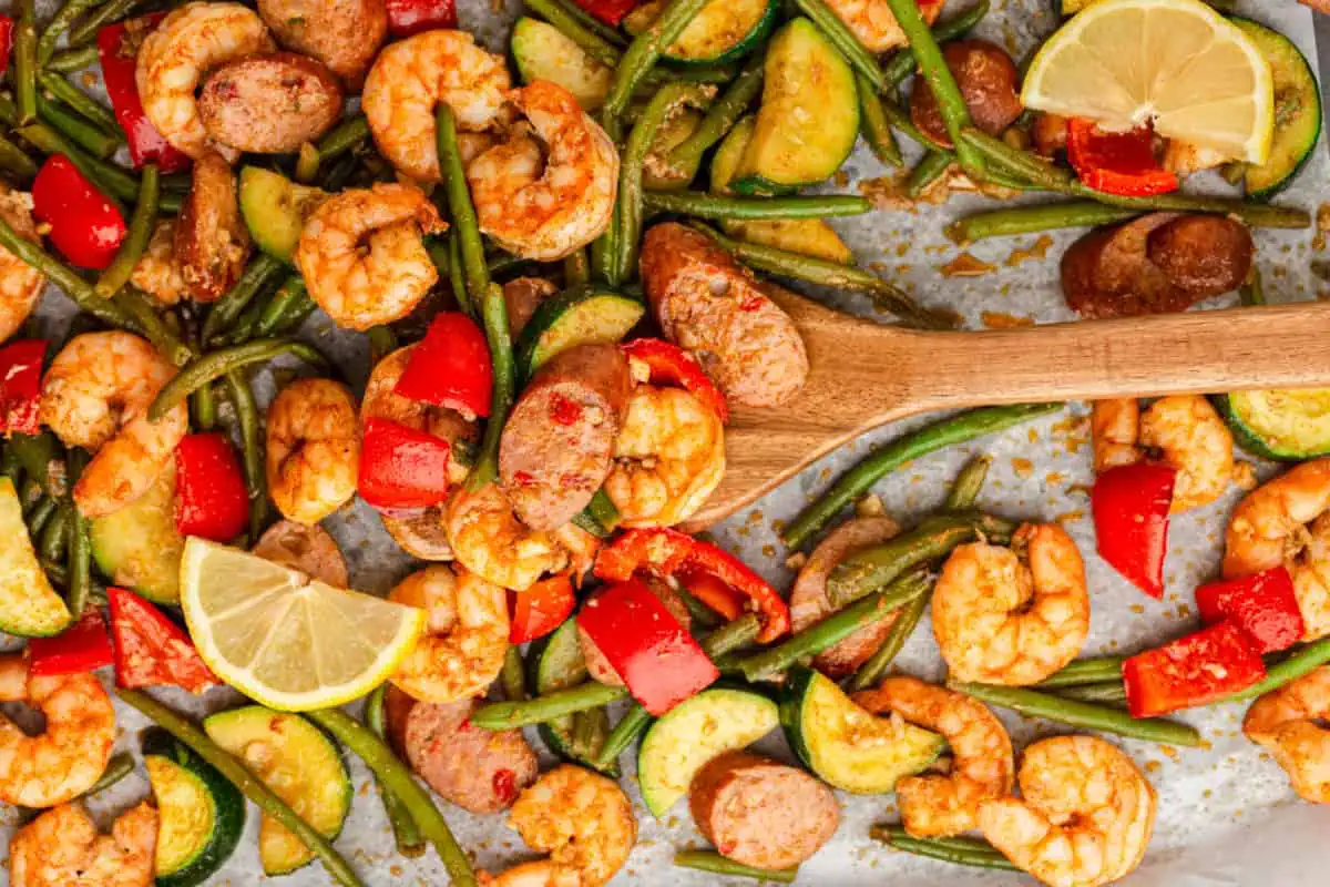 Close-up of pink Cajun shrimp and sliced andouille sausage coated in seasoning on a parchment paper and wooden spoon