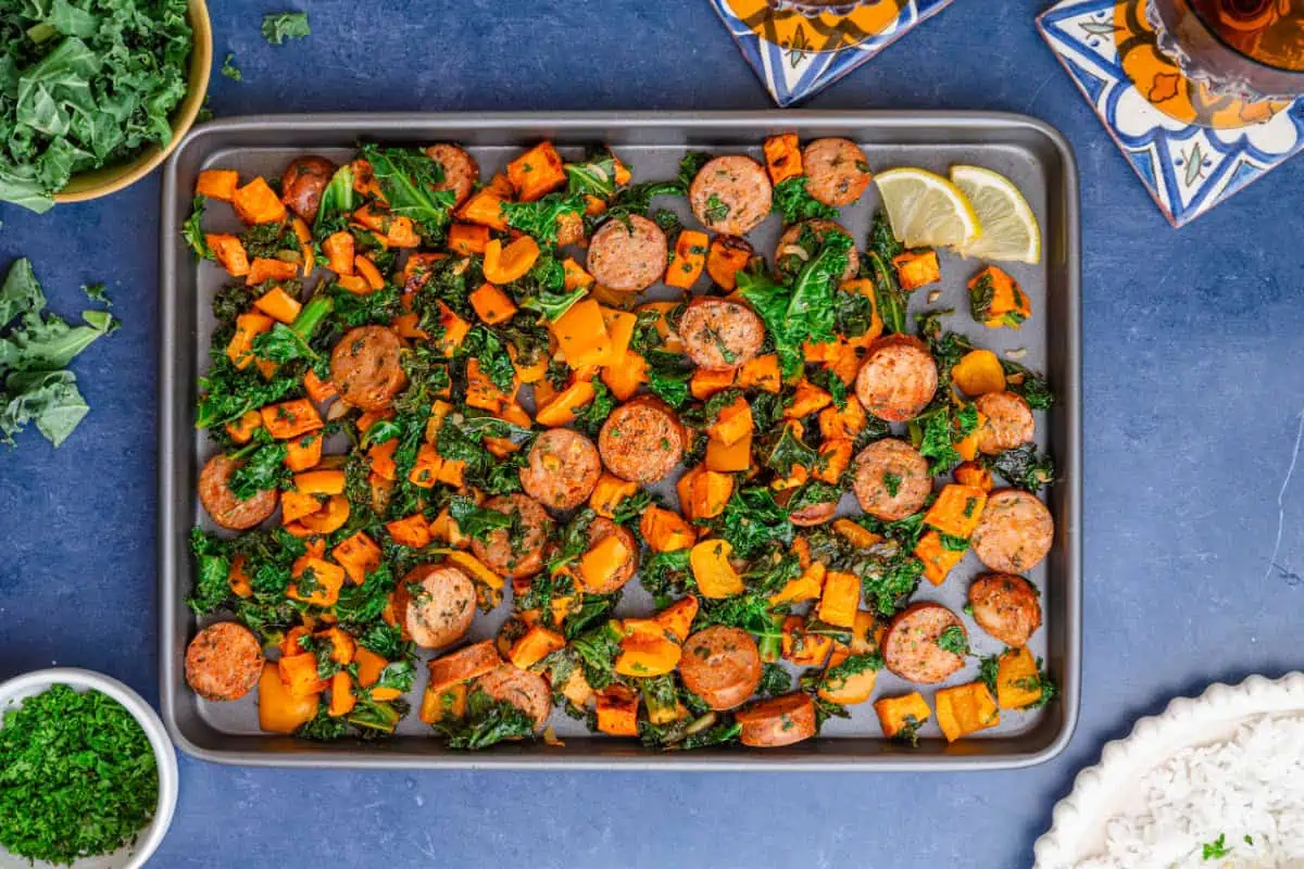 Sheet pan sausage, kale, and sweet potatoes roasted with crispy edges and lemon wedges