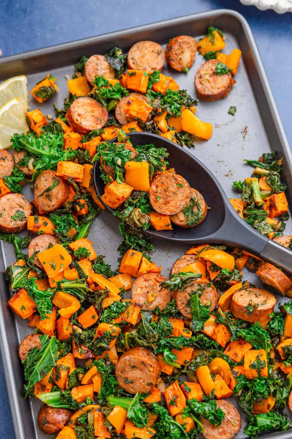 Close-up of caramelized sweet potato cubes, browned sausage, and crispy kale on a sheet pan