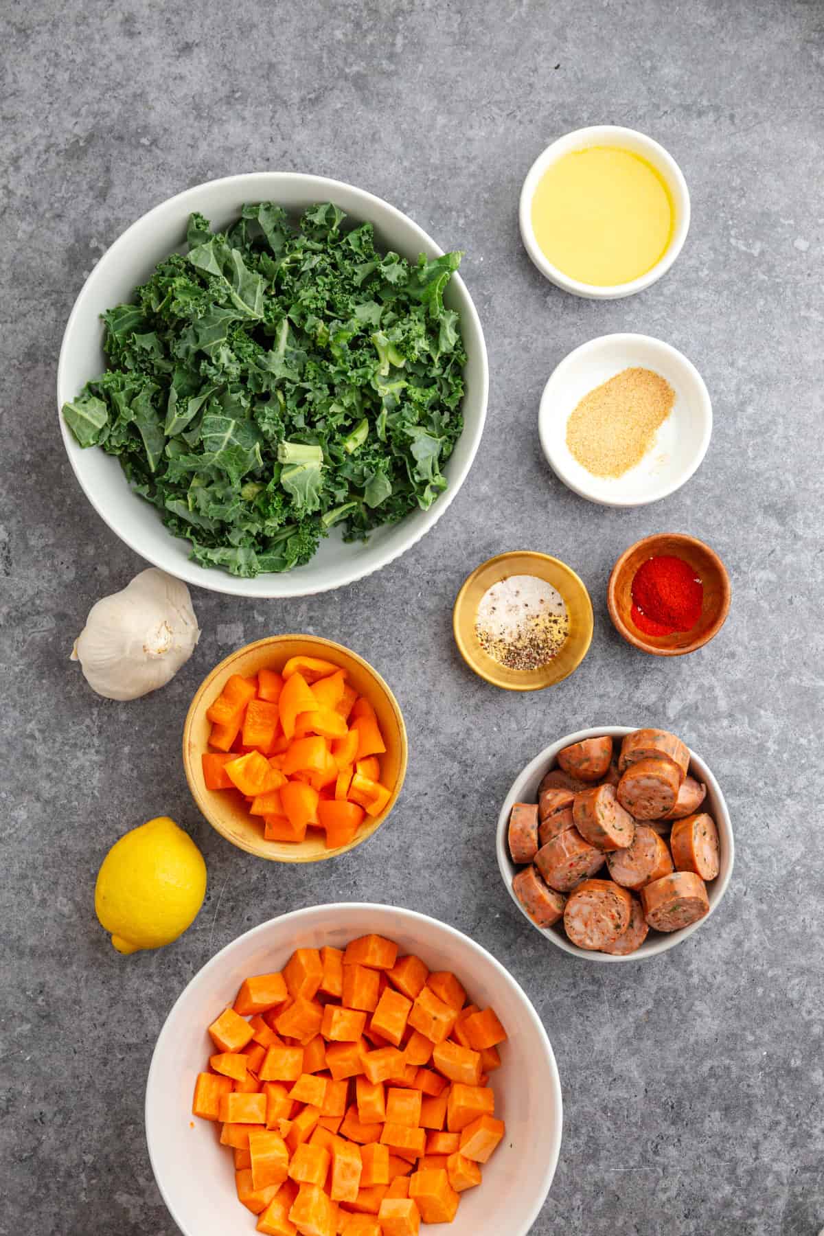 Diced sweet potatoes, chopped kale, chicken sausage, bell pepper, and lemon garlic butter laid out for a sheet pan dinner