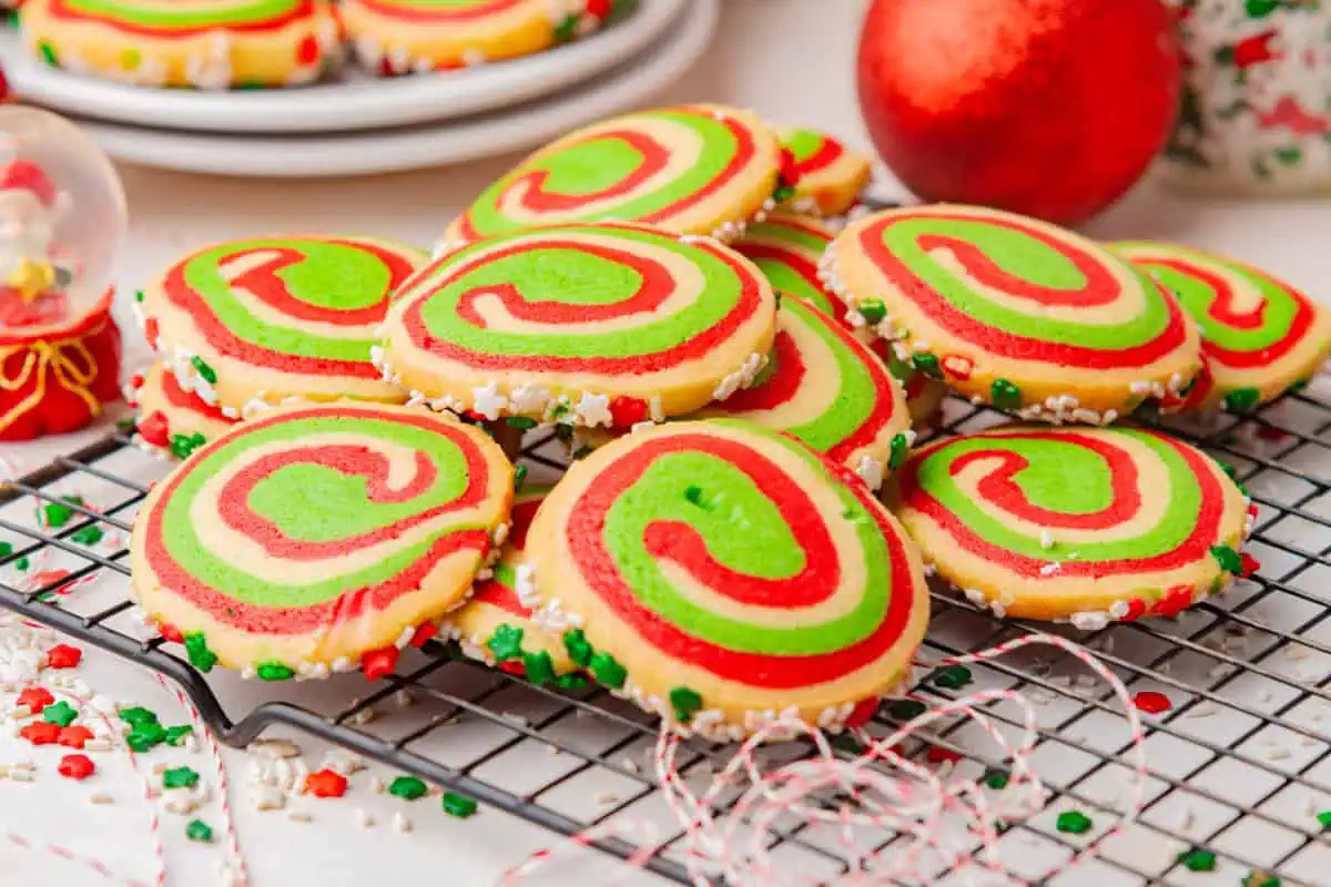 Christmas pinwheel cookies with red, green, and white spirals and sprinkle-coated edges scattered on a cooling rack