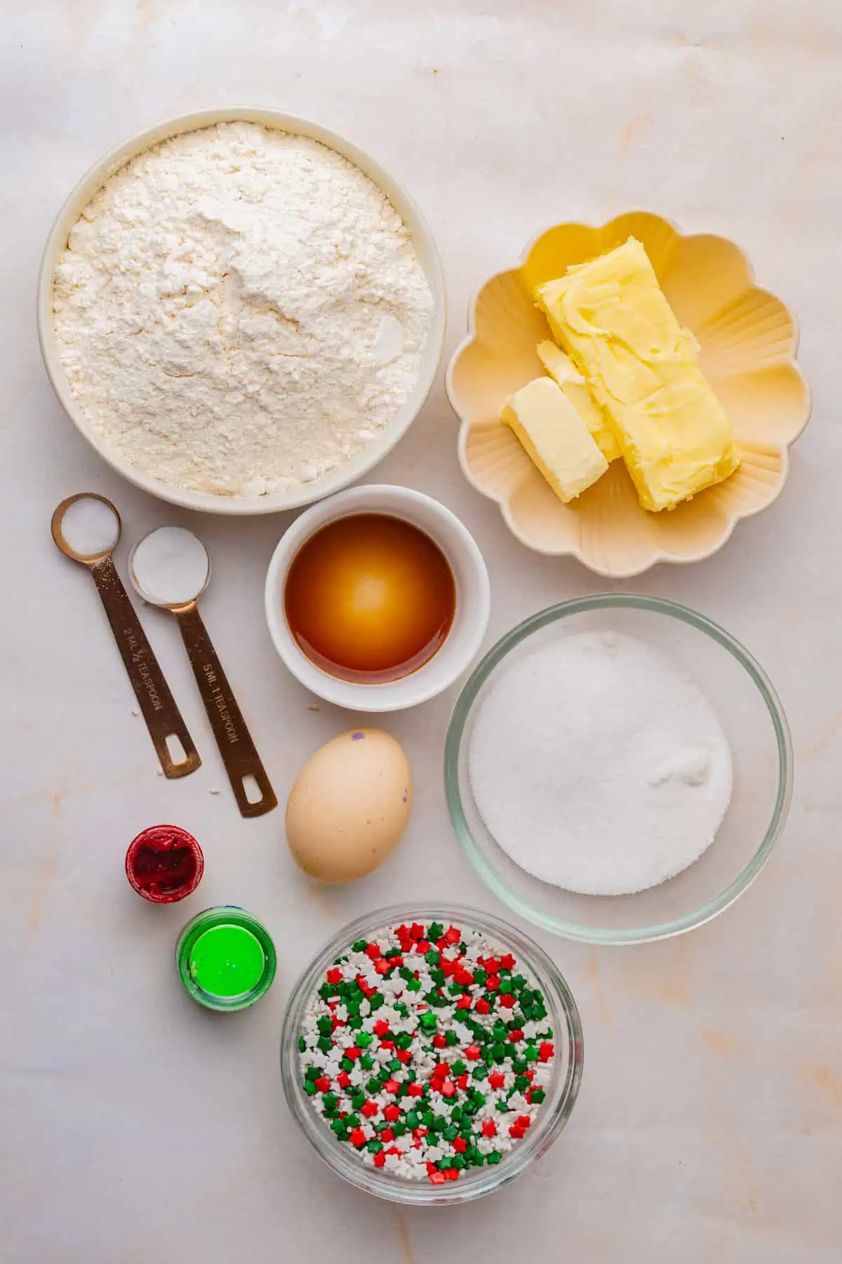 Flour, butter, sugar, egg, vanilla, red and green gel food coloring, and Christmas sprinkles laid out for Christmas pinwheel cookies