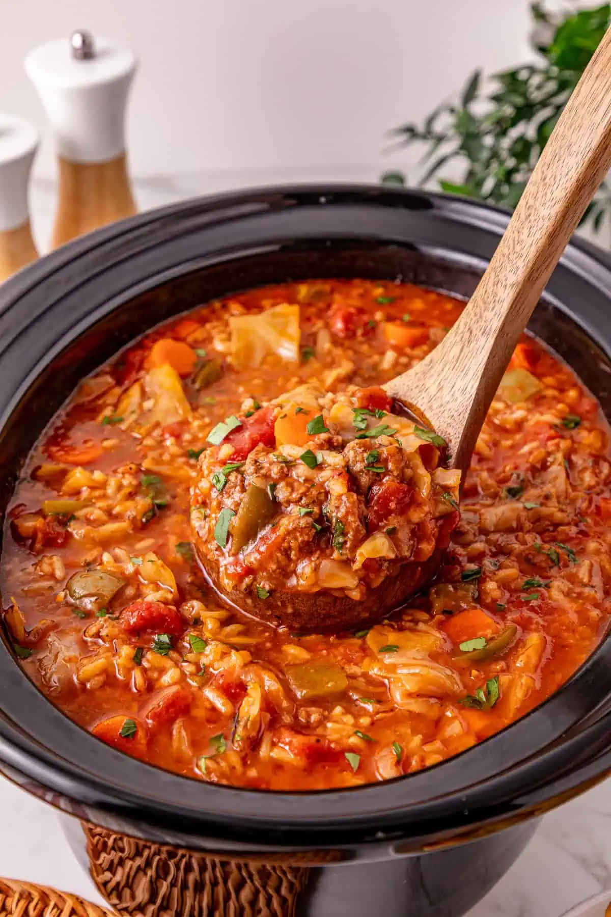 Close-up of cabbage roll soup showing tender cabbage, rice, and ground beef in a thick tomato broth on a wooden soup ladle