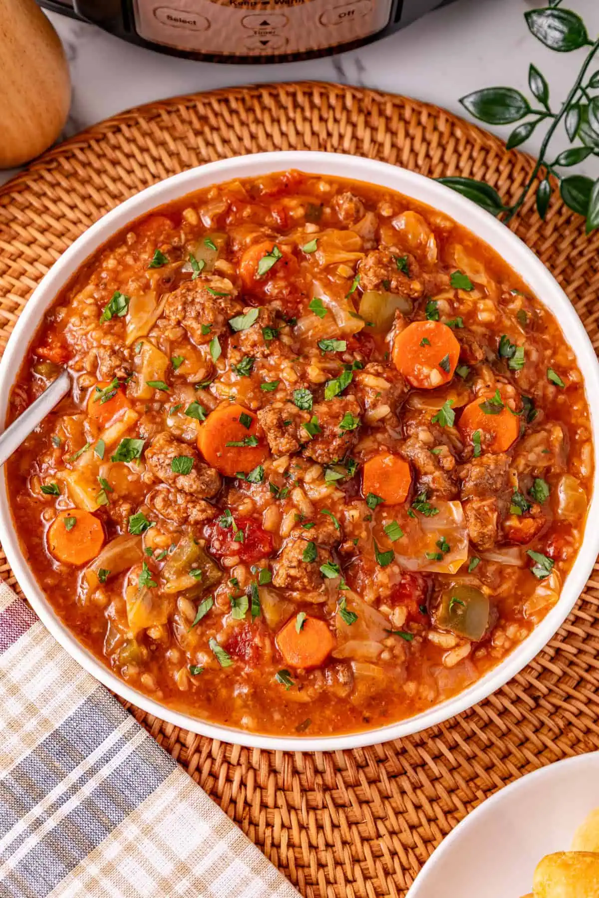 Bowl of crockpot cabbage roll soup with ground beef, cabbage, rice, and carrots in a tomato broth, topped with fresh parsley