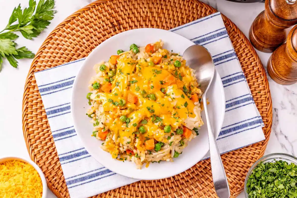 a bowl of slow cooker chicken and rice casserole garnished with fresh parsley with a white and blue striped napkin on a wicker placemat.