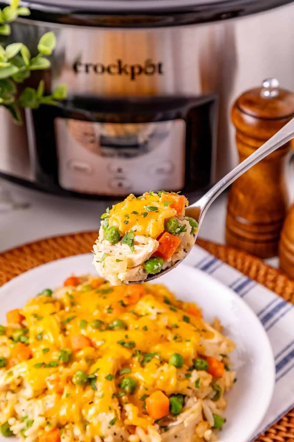 Close-up of a spoonful of cheesy chicken and rice casserole with shredded chicken, peas, and carrots
