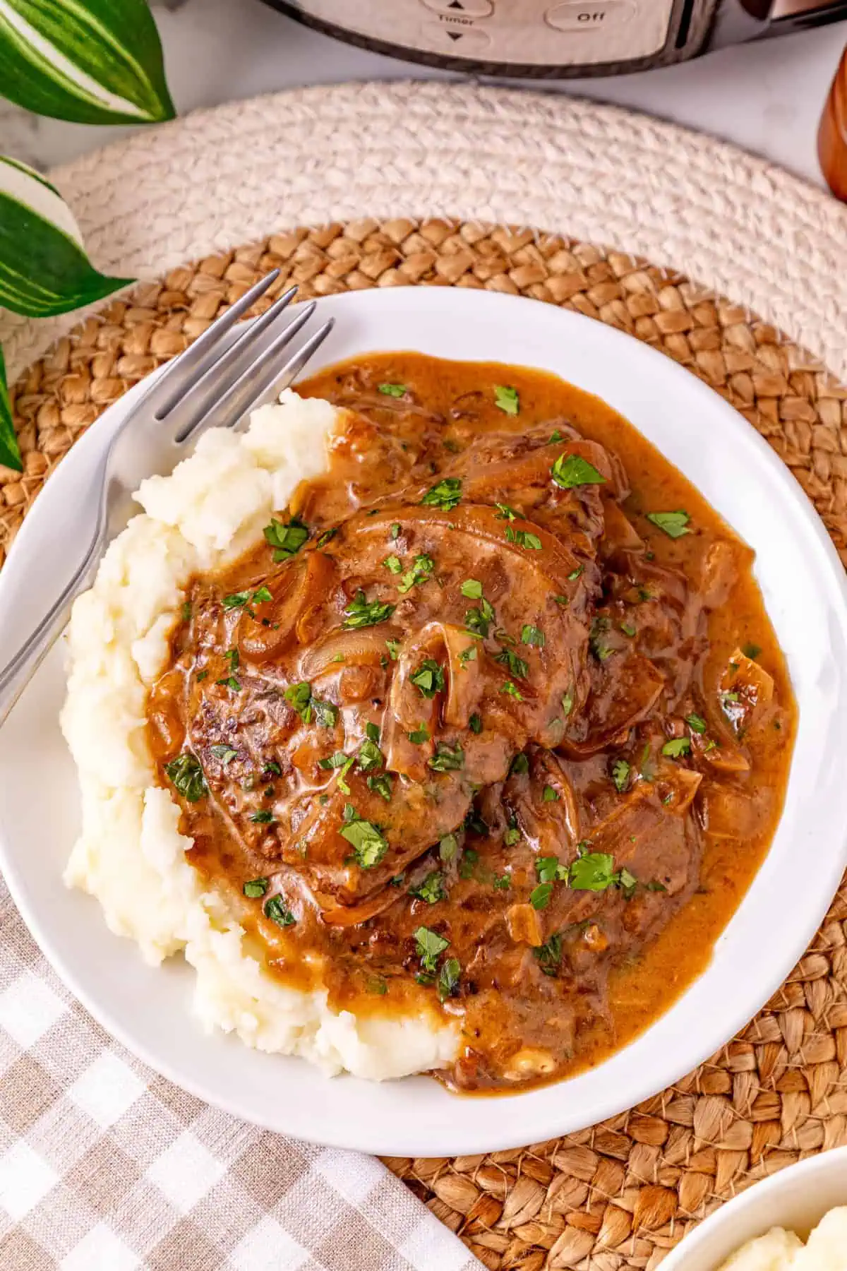Crockpot cube steak with onion gravy served over mashed potatoes and topped with fresh parsley