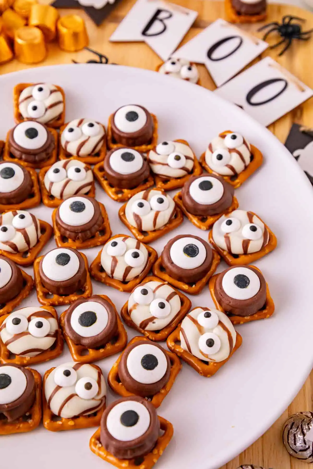 Halloween monster eye pretzels with one-eyed Rolo monsters and two-eyed Hershey’s Hug monsters on a white ceramic plate.